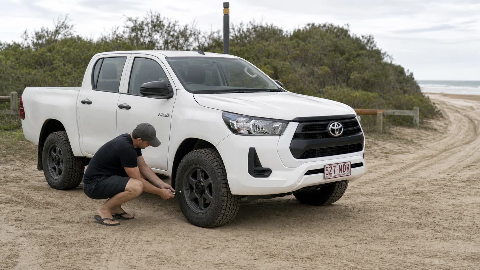 White Toyota HiLux N80 parked at a Queensland beach access while its owner checks an all-terrain tyre